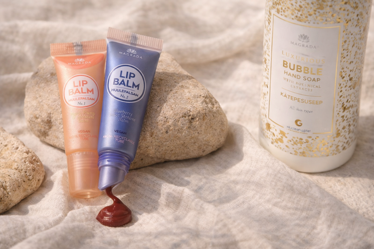 Lipbalms van Magrada Organic Cosmetics in twee varianten en een handzeep, gepresenteerd op natuurlijke stenen en linnen stof in een rustige setting