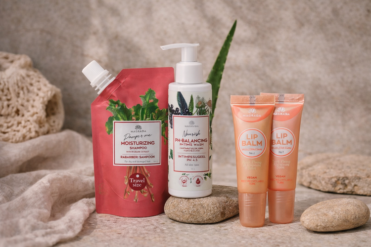 Natuurlijke verzorgingsproducten van NatuurlijkZeepje in een lifestyle setting: travel size rabarber shampoo, pH-balancerende intimate wash en twee vegan lip balms, gestyled op natuursteen met linnen en zacht daglicht.